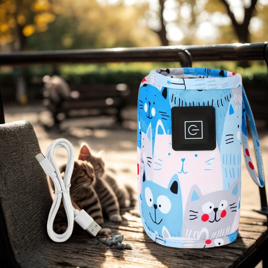 Chauffe biberon nomade bleu sur un banc de parc avec un câble USB et deux chats derrière.