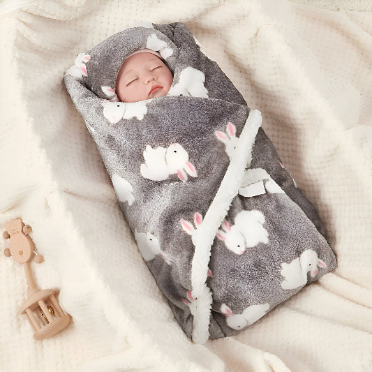 Un bébé entouré de sa couverture grise avec des lapins dans un lit à côté d'un jouet en bois