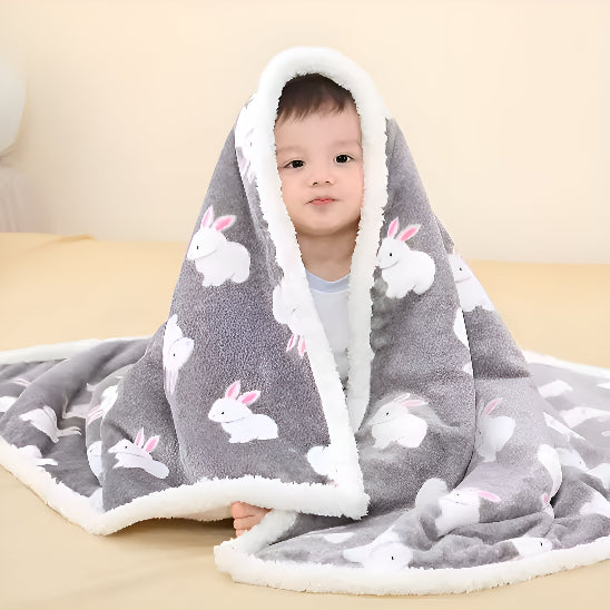 Un bébé assis en dessous d'une couverture grise avec des lapins dessus, un lit