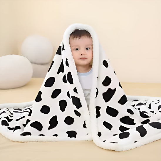 Un bébé assis sur un lit avec une couverture blanche avec des taches noir dessus lui