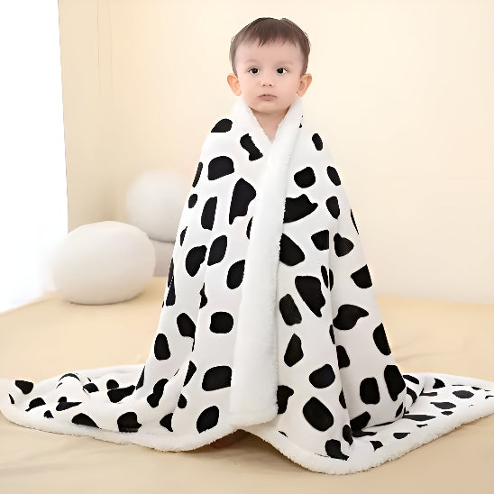 Un bébé debout sur un lit avec une couverture blanche avec des taches noir qui l'entoure