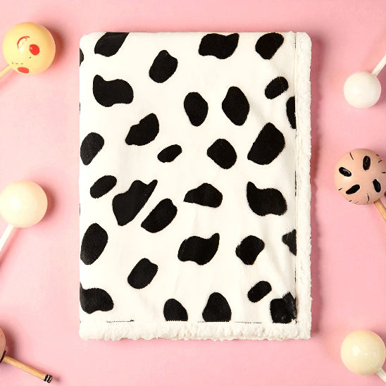 Une couverture blanche avec des taches noire, dessus une table rose avec des jouets de bébé