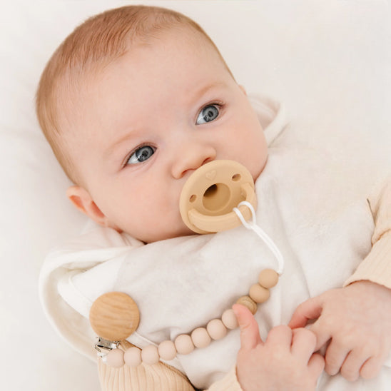 Un bébé couché dans son lit avec une tétine dans la bouche, attaché à une accroche tetine EasyBeech™ sur son chandail.