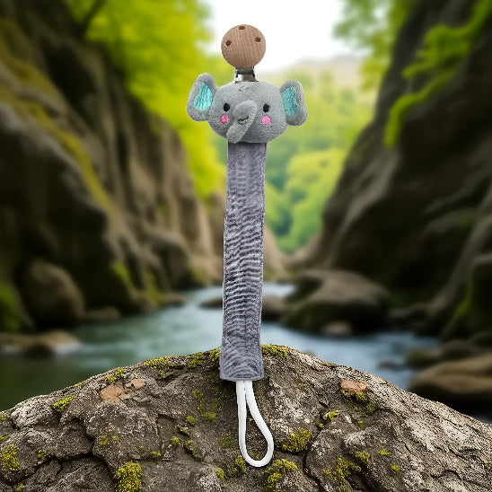 Attache tétine en forme de tête d'éléphant sur une roche devant un ruisseau entre deux montagnes.