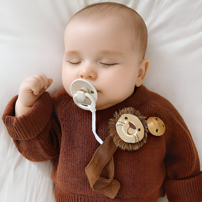 Un bébé dormant dans une doudou blanche avec un chandail brun avec une susse accrocher sur une attache tétine en forme de tête de lion.