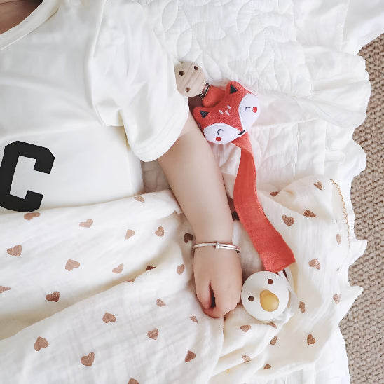  Un bébé couché dans une doudou avec des cœurs avec une attache tétine orange