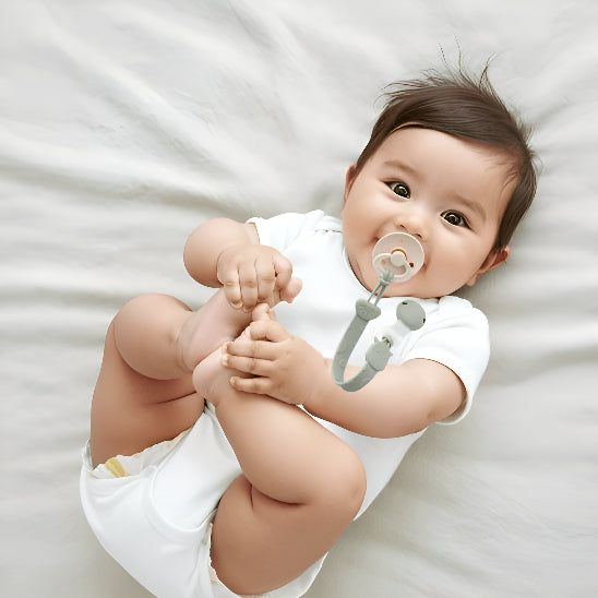 Un bébé couché dans un lit jouent avec ses pieds avec une suce attaché par une attache tétine