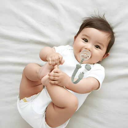 Un bébé couché dans un lit jouent avec ses pieds avec une suce attaché par une attache tétine