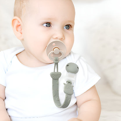 Un bébé avec une suce accroché par une attache tétine sur un chandail blanc devant un mur blanc