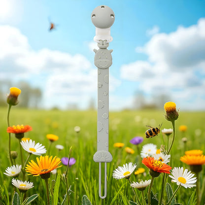 Une attache tétine devant un paysage avec des fleurs de différente couleur et une abeille avec un ciel bleu et des nuages