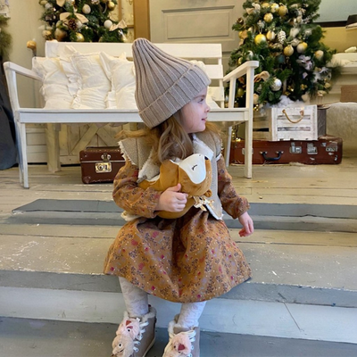 Un enfant portant un bonnet pour bebe au tricot gris, assis par terre.