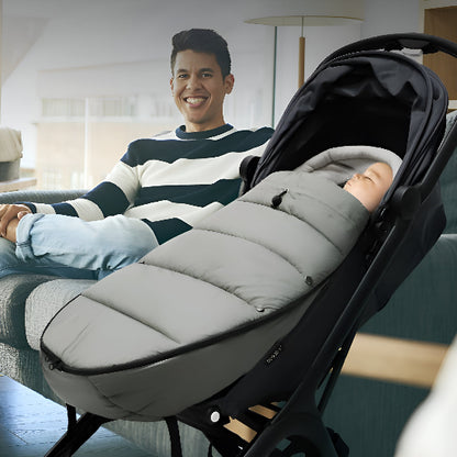 Un papa sourit et regarde un bébé dans une chanceliere grise dans une poussette dans un salon.