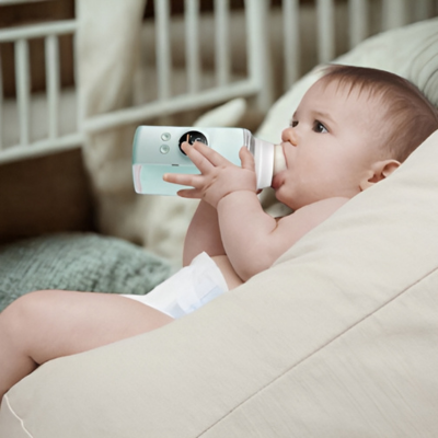 Un bébé tenant un chauffe-biberon dans une chambre d'enfant.