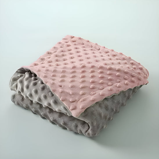 Une couverture grise et rose pliée sur une surface blanche 