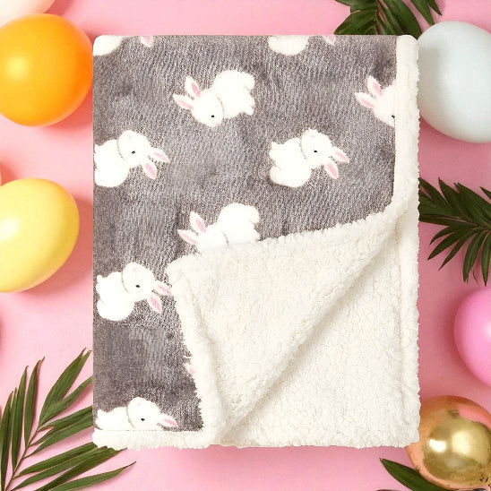 Une couverture grise avec des lapins pliée, dessus une table rose avec des ballons et des plantes