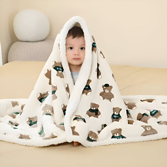 Un bébé assis sur un lit avec une couverture blanche avec des oursons dessus lui 