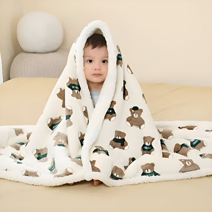 Un bébé assis sur un lit avec une couverture blanche avec des oursons dessus lui 