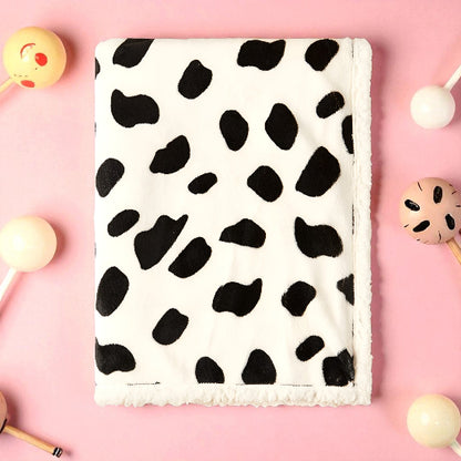 Une couverture blanche avec des taches noire, dessus une table rose avec des jouets de bébé