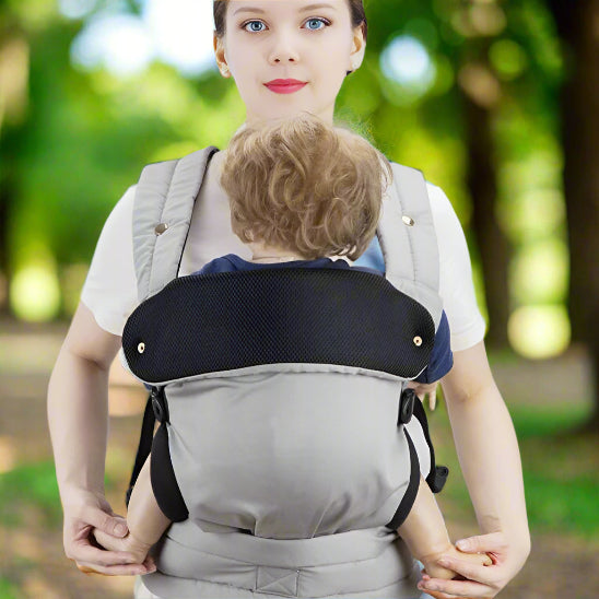 Une maman portant un bébé dans un porte bébé physiologique Ergofashion™ gris, dans un parc.
