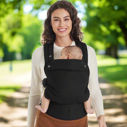 Une maman portant un bébé dans un porte bébé physiologique Ergofashion™ noir, dans un parc.